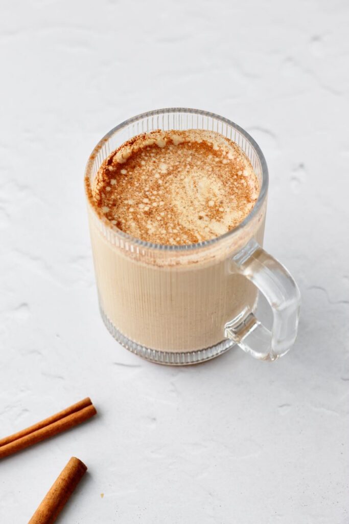 Cinnamon roll protein latte with cinnamon sticks in background