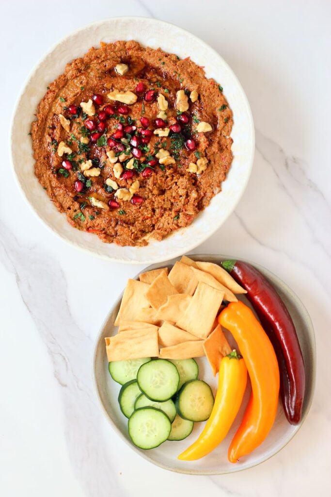 Muhammara with plate of pita chips, cucumbers, and peppers.