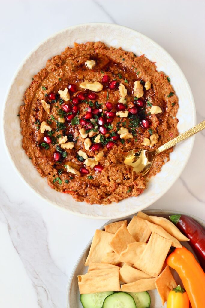 Muhammara with plate of pita chips, cucumbers, and peppers.