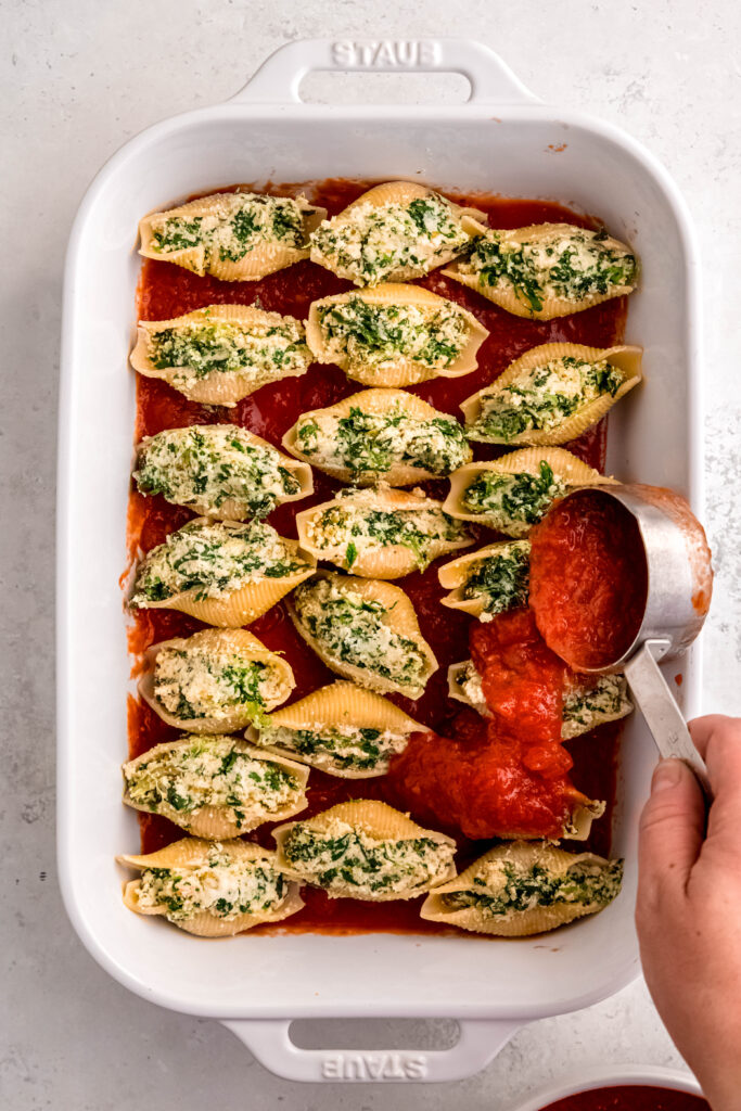 Pouring marinara over stuffed shells