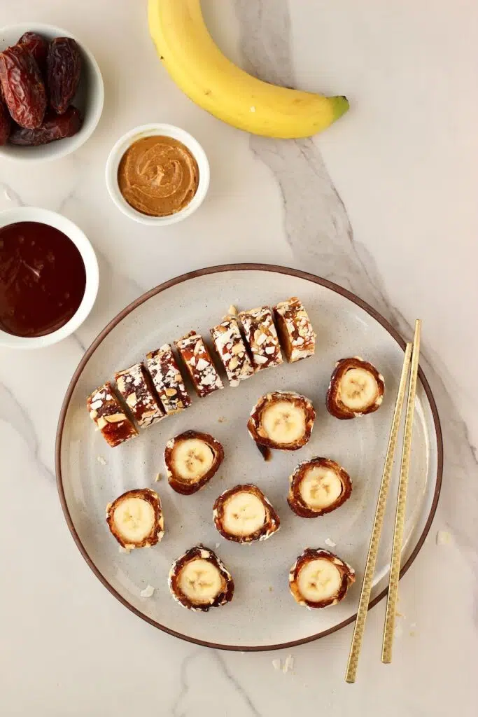 Banana sushi on a plate with ingredients next to plate