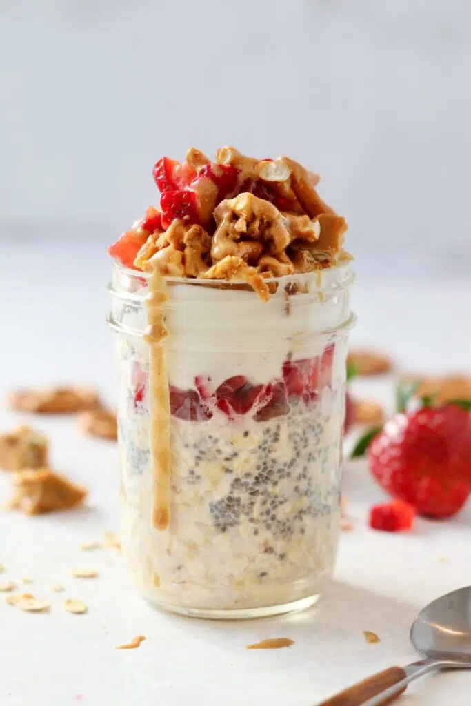 Strawberry overnight oats in jar with pretzels crumbles and nut butter drizzled on top