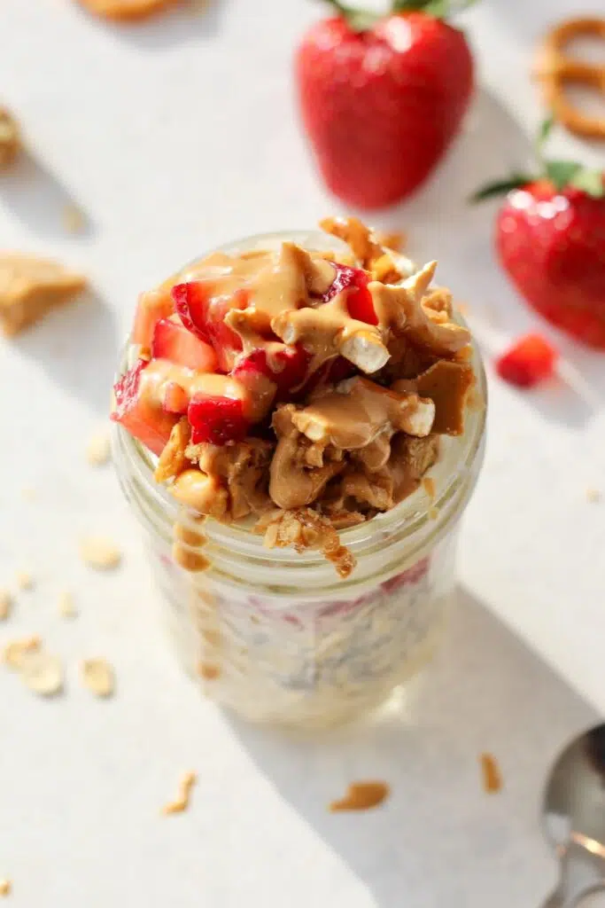 Strawberry overnight oats in jar with pretzels crumbles and nut butter drizzled on top