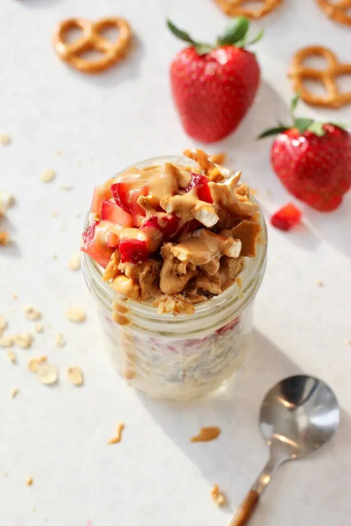 Strawberry overnight oats in jar with pretzels crumbles and strawberries in background.