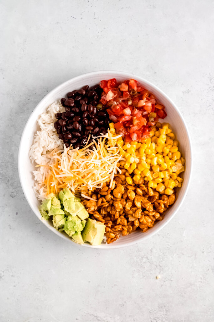 Rice, tempeh, black beans, corn, pico, avocado, and cheese in bowl