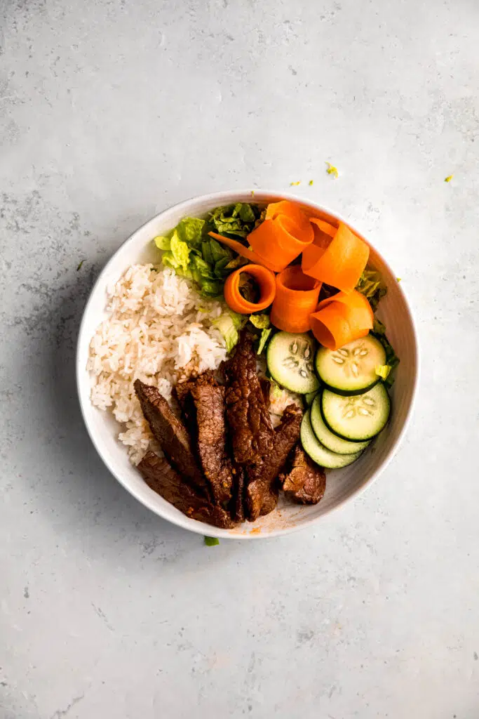 White rice, steak, lettuce, and slivered carrots in white bowl