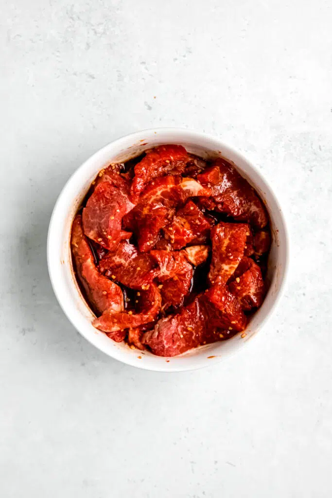 Steak marinating in white bowl