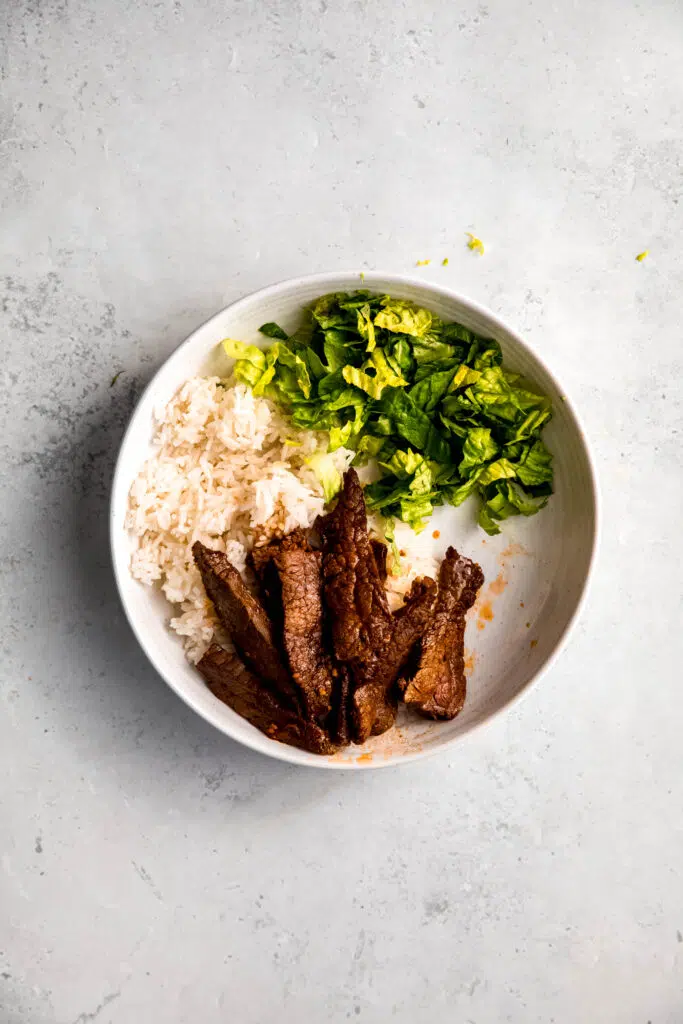 White rice, steak, and lettuce in white bowl