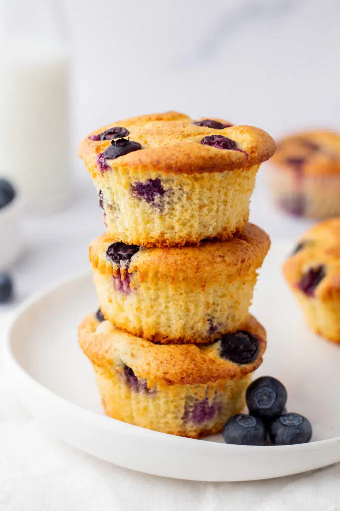 3 blueberry protein muffins stacked on top of each other with fresh blueberries around.