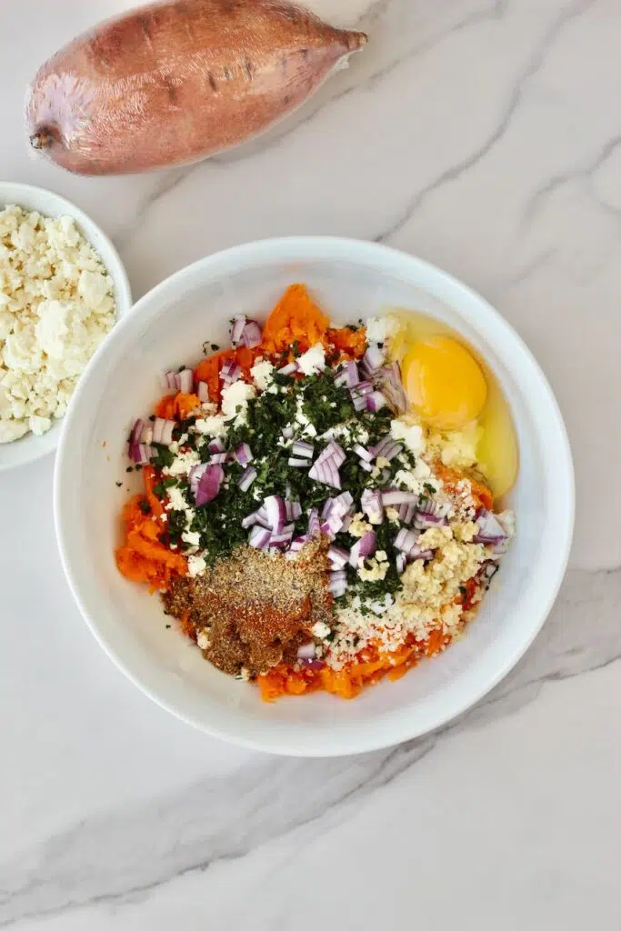 Ingredients added to mashed sweet potato in white bowl