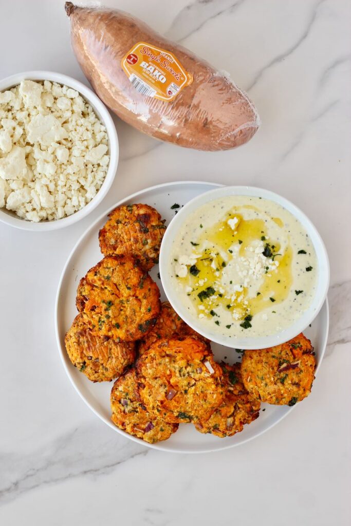 Sweet potato patties with feta dip on  white plate and feta cheese and a uncooked sweet potato in background