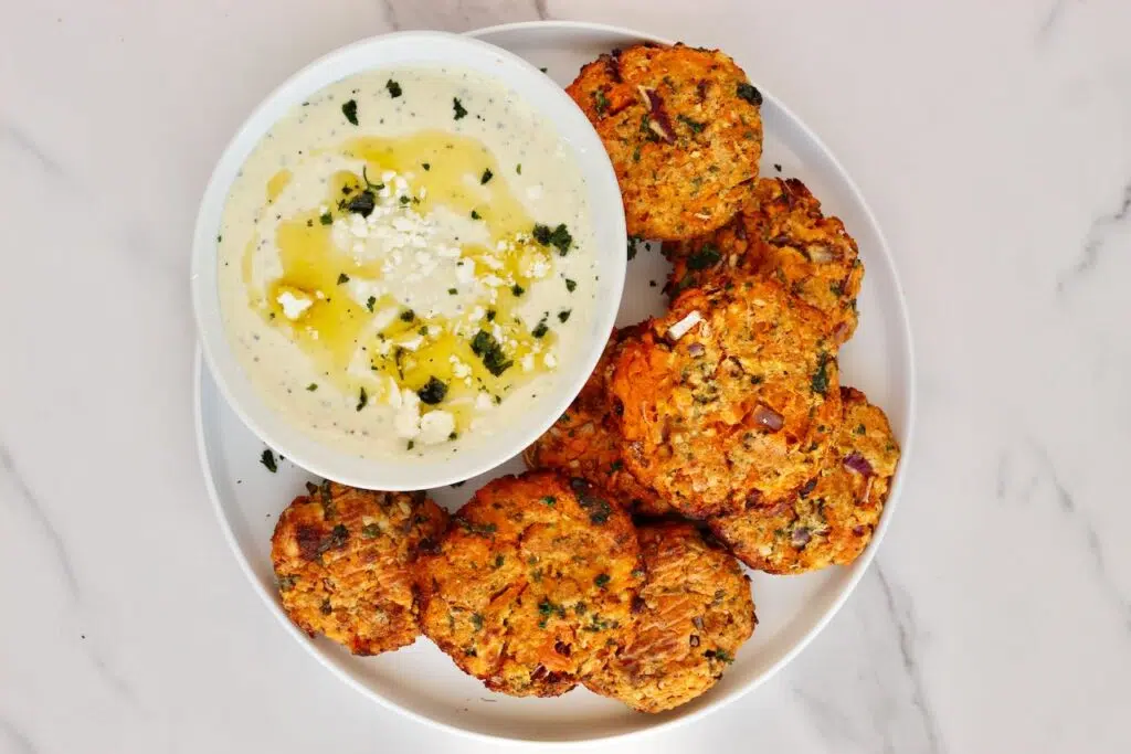 Sweet potato patties on white plate with whipped feta dip in white bowl