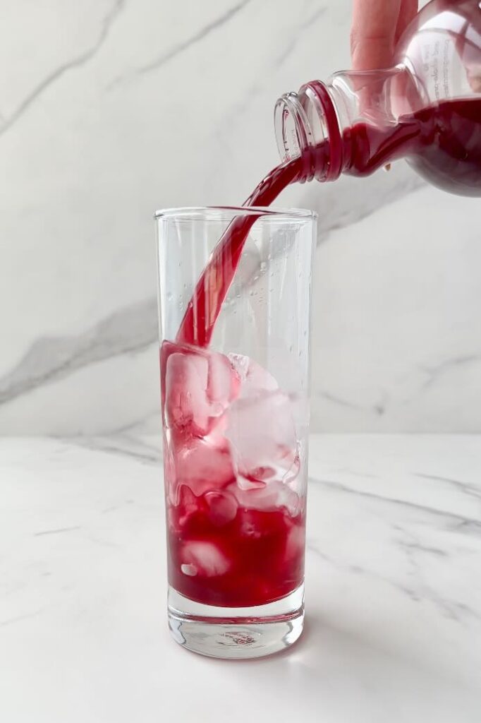 Pouring pomegranate juice in glass with ice