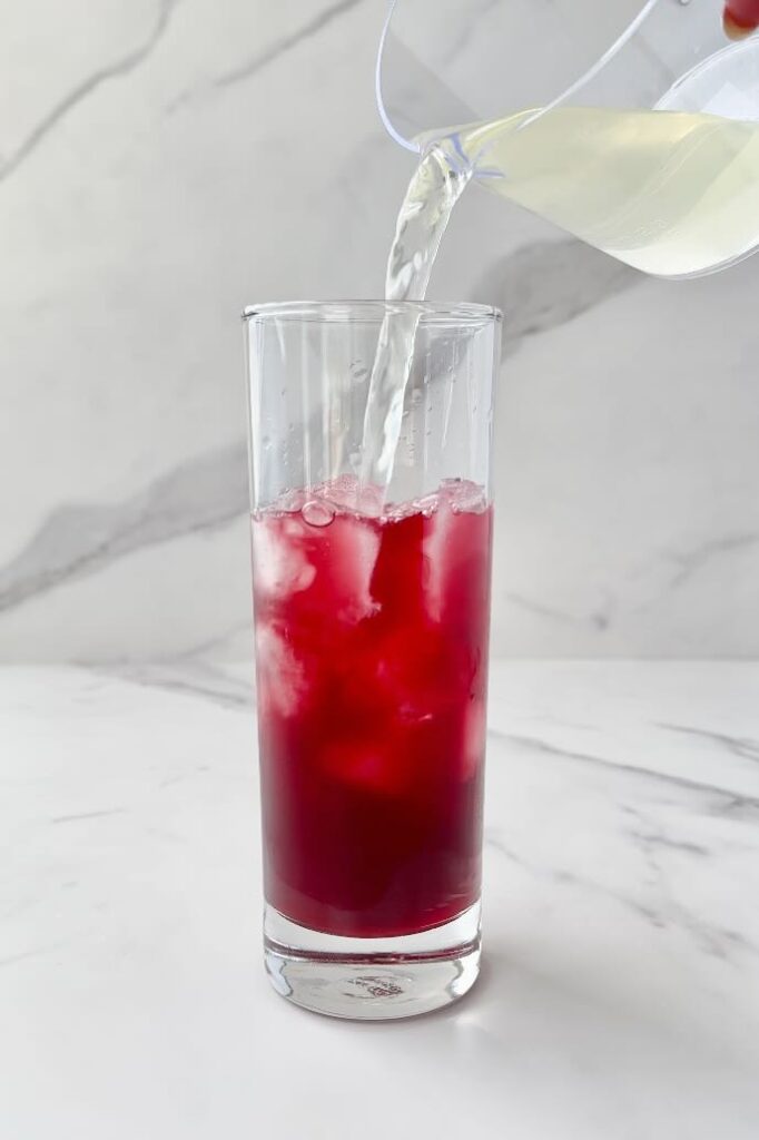 Pouring coconut water into glass with pomegranate juice and ice