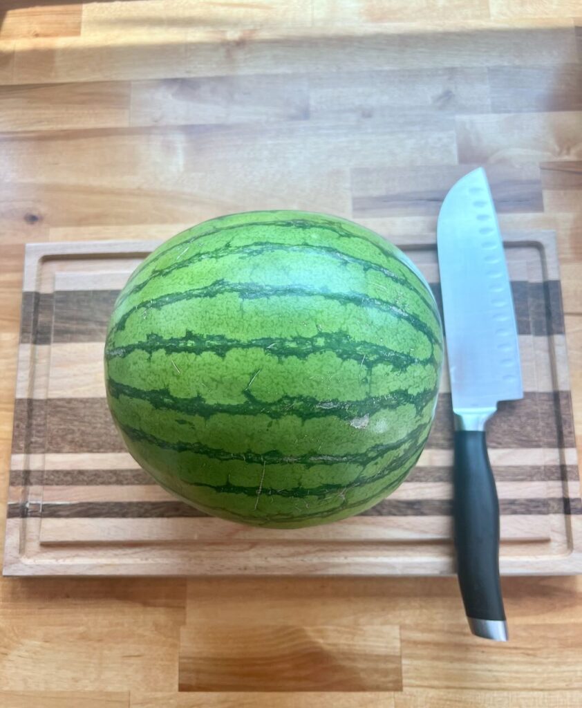 Whole watermelon on cutting board with large knife