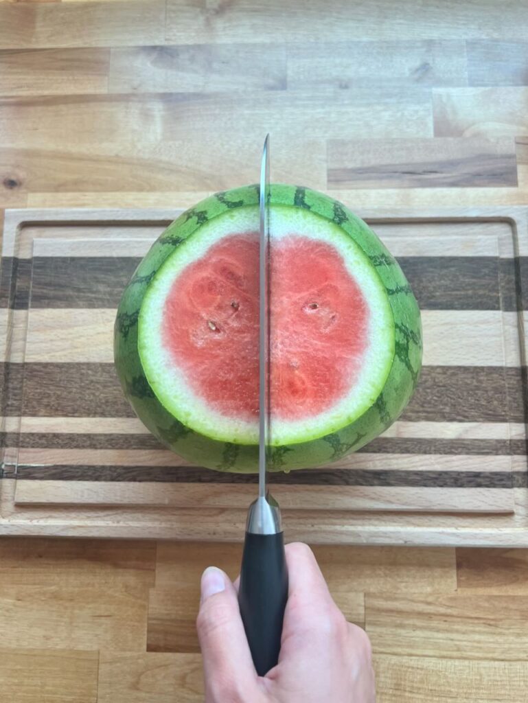 Knife cutting watermelon in half on cutting board