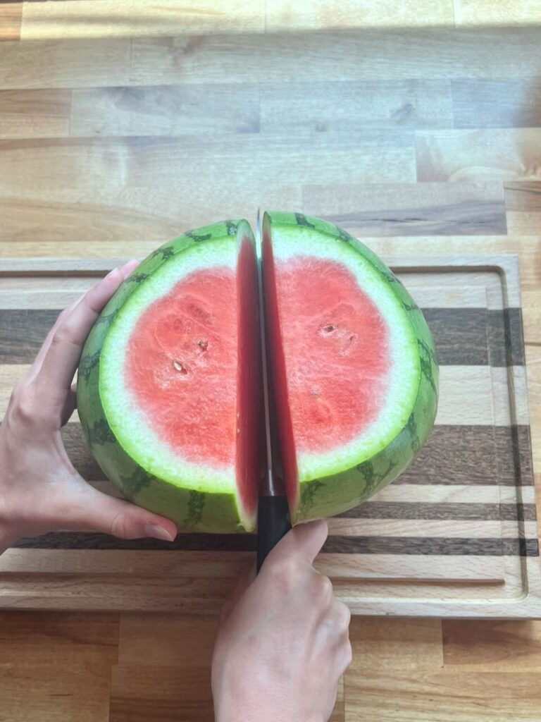 Knife cutting watermelon in half on cutting board