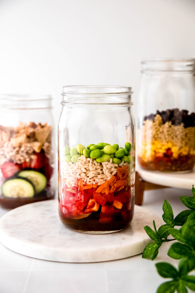 Mason jar with edamame on top of grains, veggies, and dressing