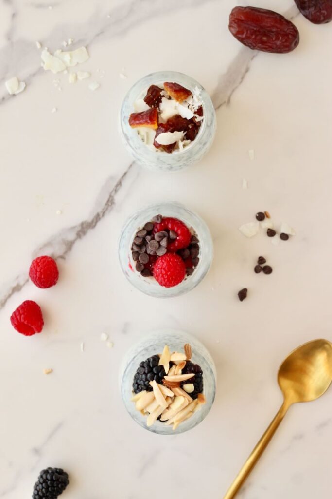 Overhead shot of 3 types of chia pudding in jars with different toppings and gold spoon