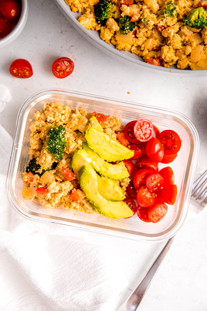 Tofu scramble in meal prep container topped with avocado and tomatoes
