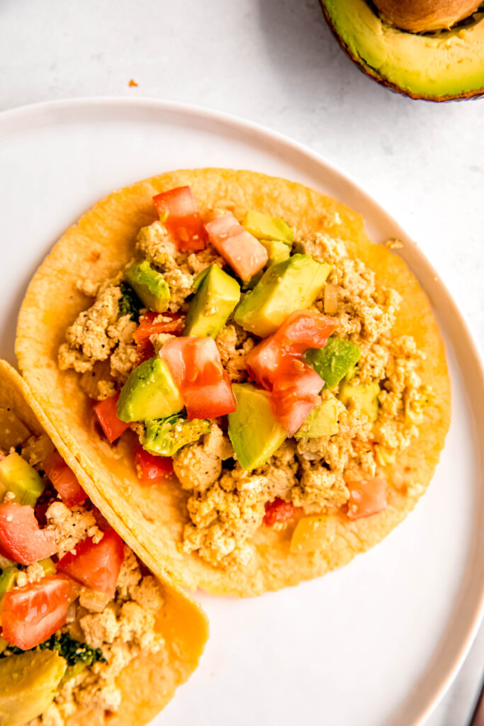 Tofu scramble in corn tortillas topped with avocado and tomatoes
