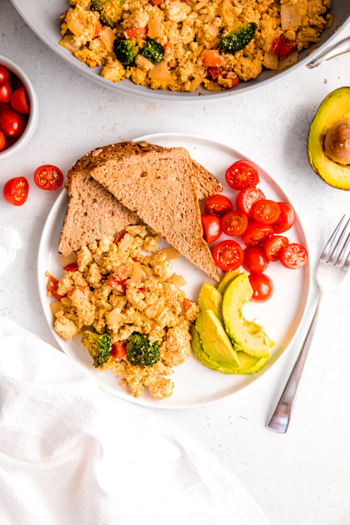 Tofu scramble with toast, avocado, and tomatoes on white plate