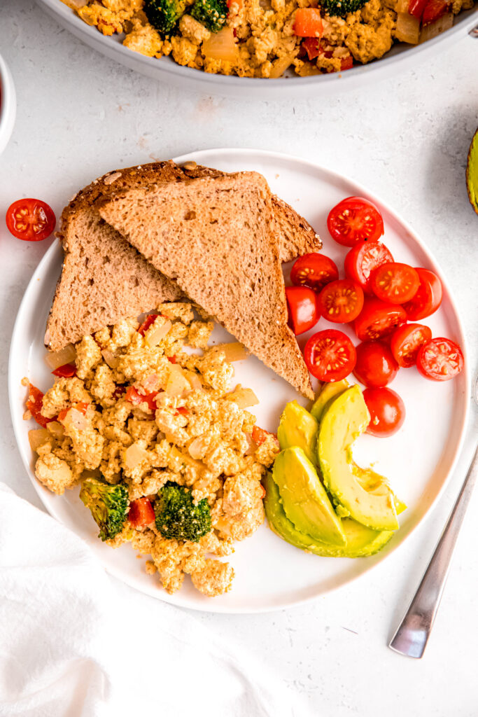 Tofu scramble with toast, avocado, and tomatoes on white plate
