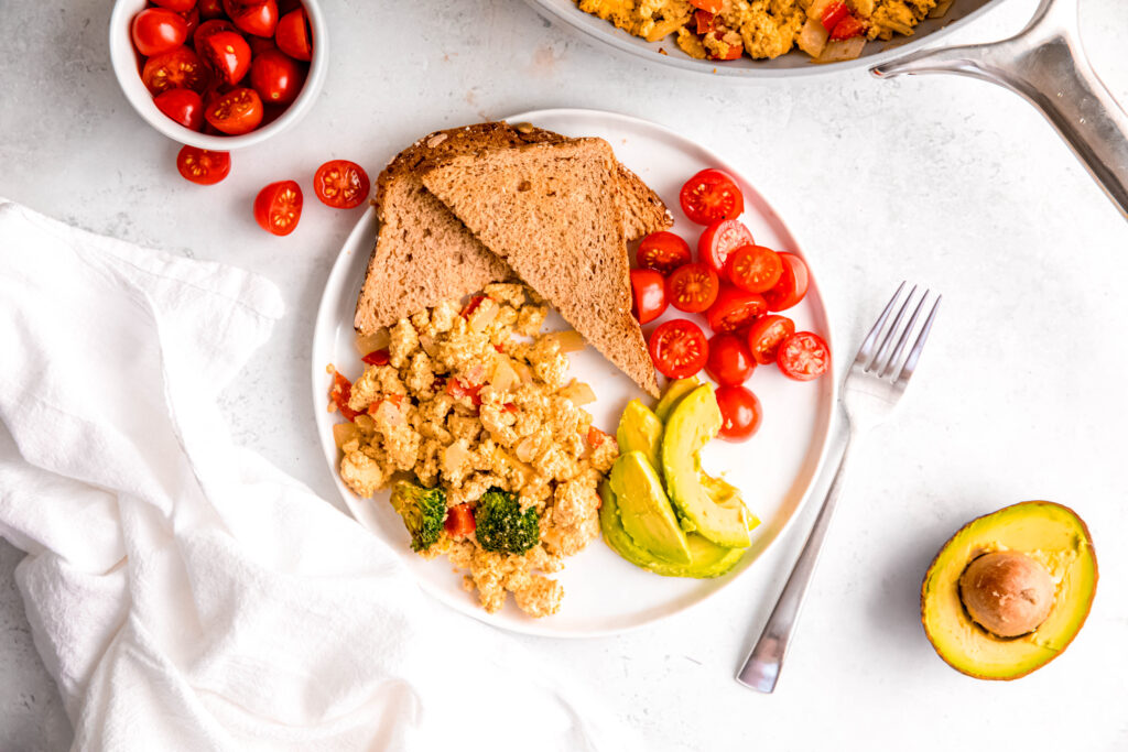 Tofu scramble with toast, avocado, and tomatoes on white plate