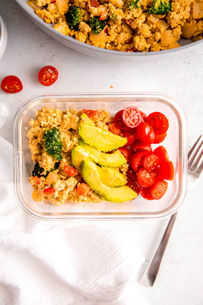 Tofu scramble in meal prep container topped with avocado and tomatoes
