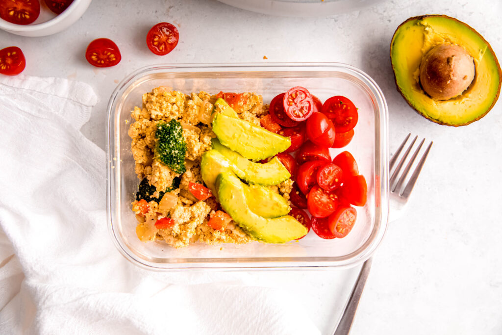 Tofu scramble in meal prep container topped with avocado and tomatoes