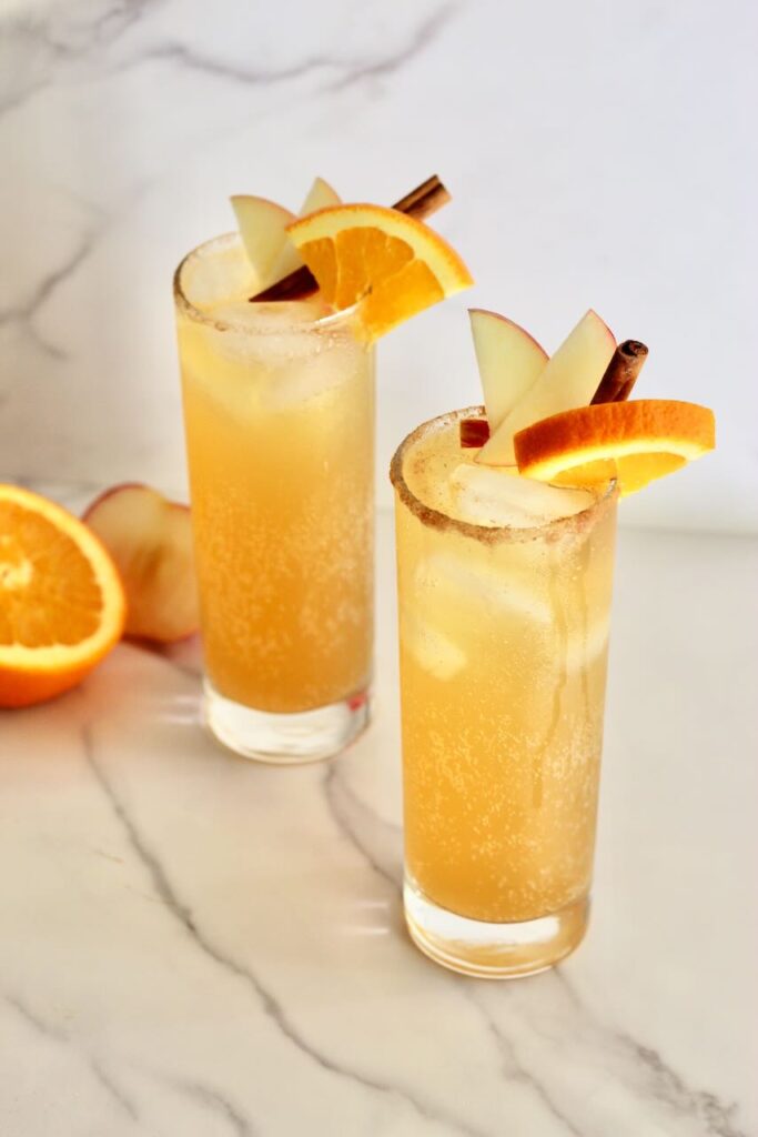Two apple cider mocktails with orange half in background