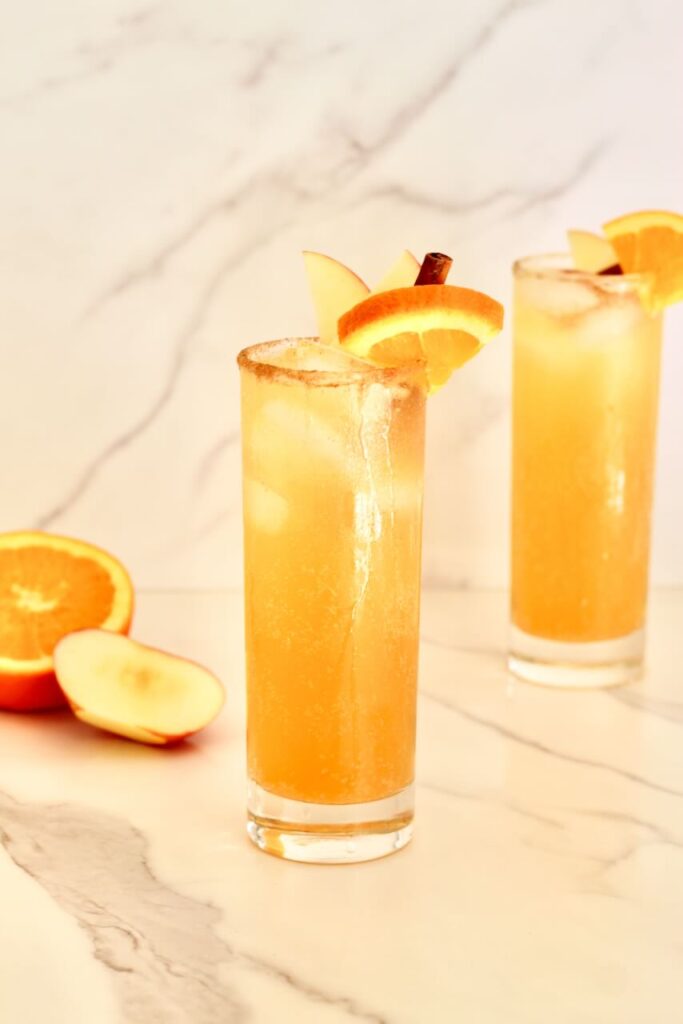 Two apple cider mocktails with orange slice, apple slice and cinnamon stick garnish