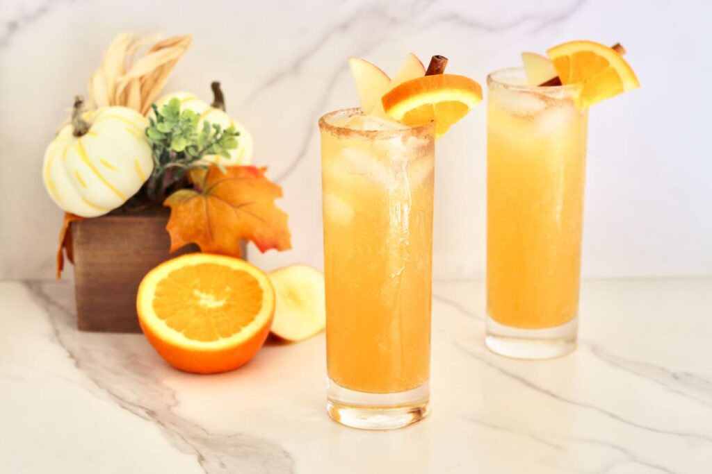 Two apple cider mocktails with fall decor in background