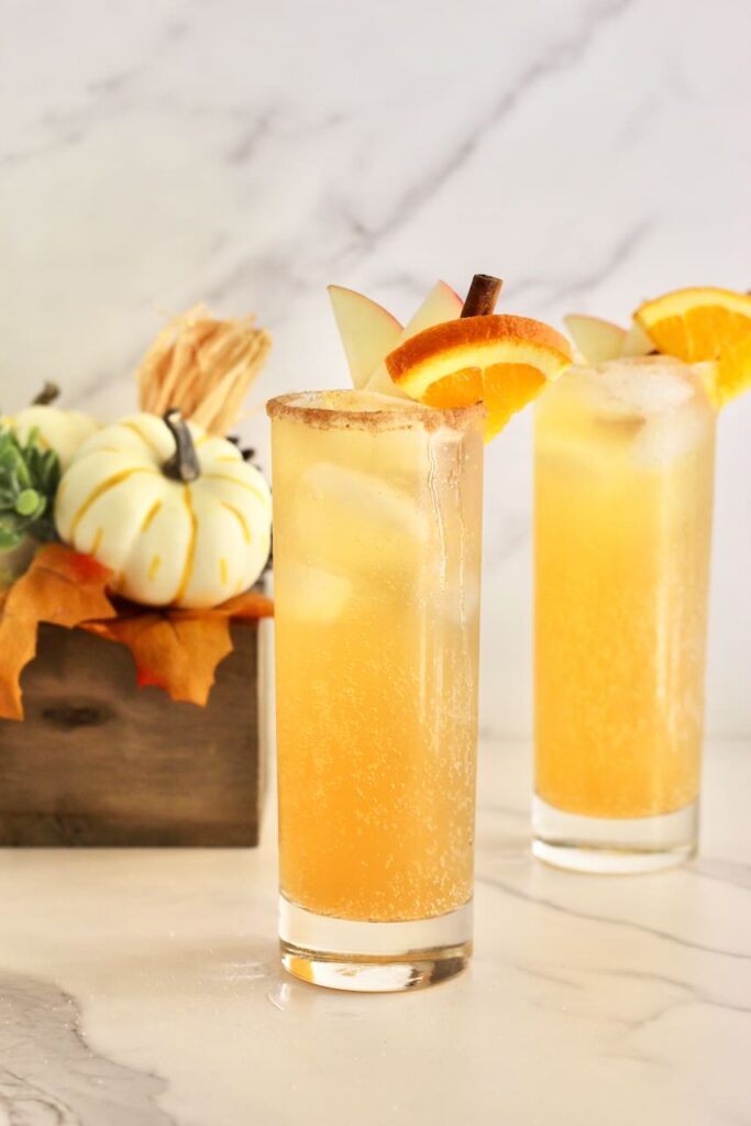 Two apple cider mocktails with pumpkin in background
