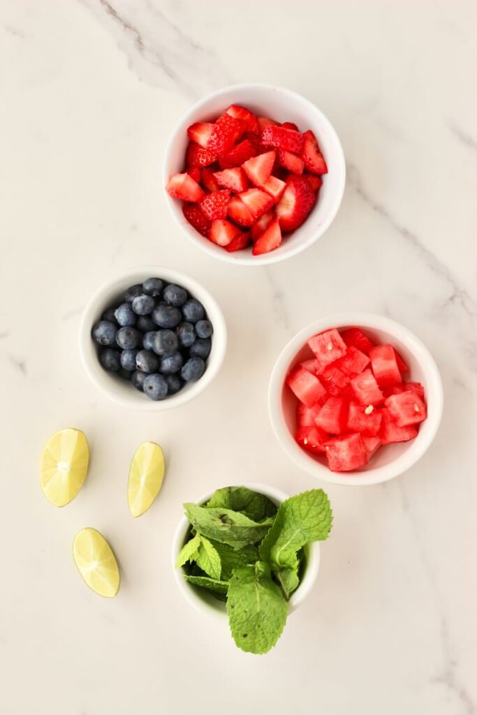 Strawberries, blueberries, and watermelon in separate bowls, plus mint and lime wedges