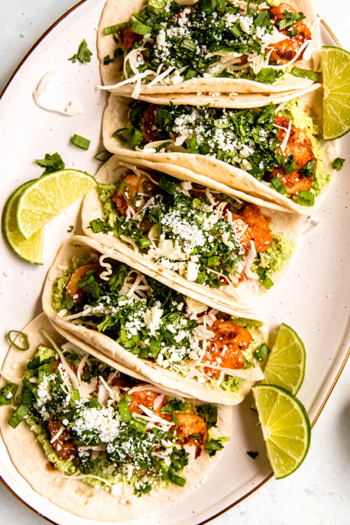 Shrimp Tacos with Edamame Guac and lime wedges on white plate 
