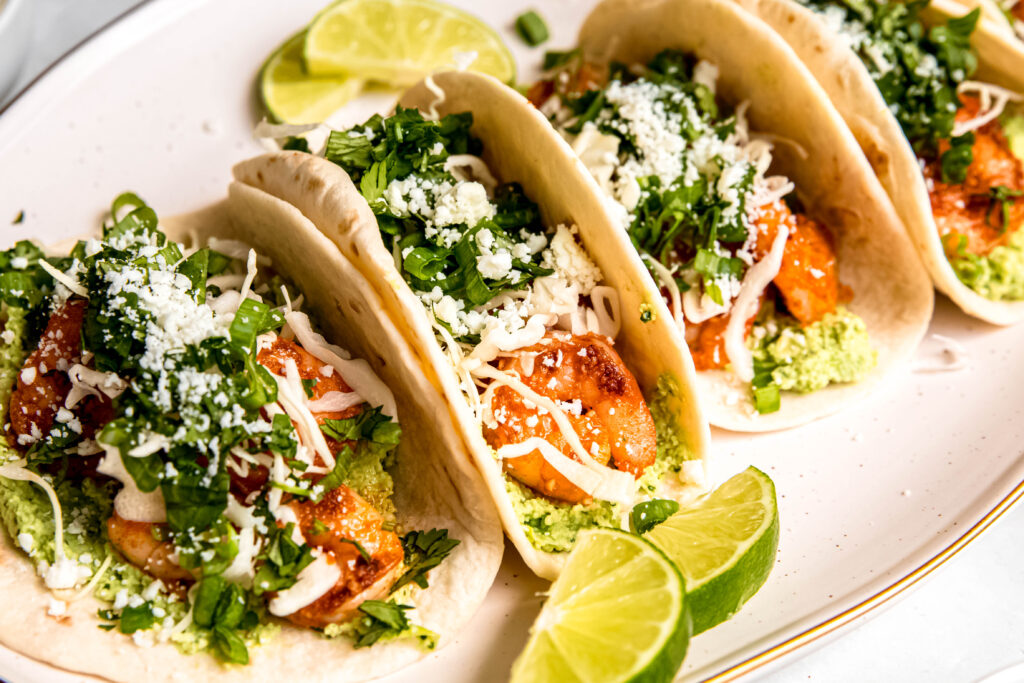 Healthy Shrimp Tacos with Edamame Guac and lime wedges on white plate 
