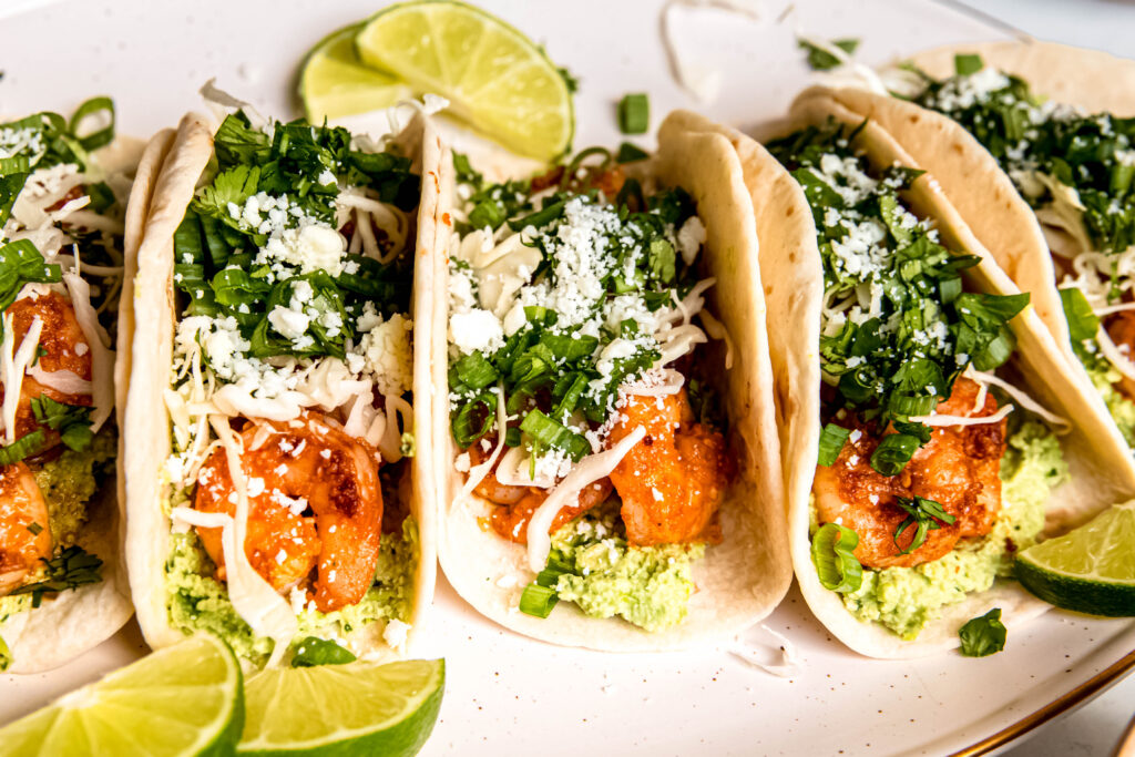 Shrimp Tacos with Edamame Guac and lime wedges on white plate 