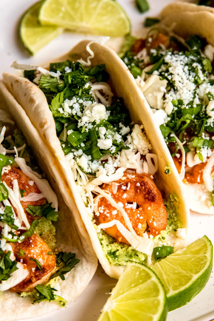 Close up of Shrimp Tacos with Edamame Guac and lime wedges on white plate 