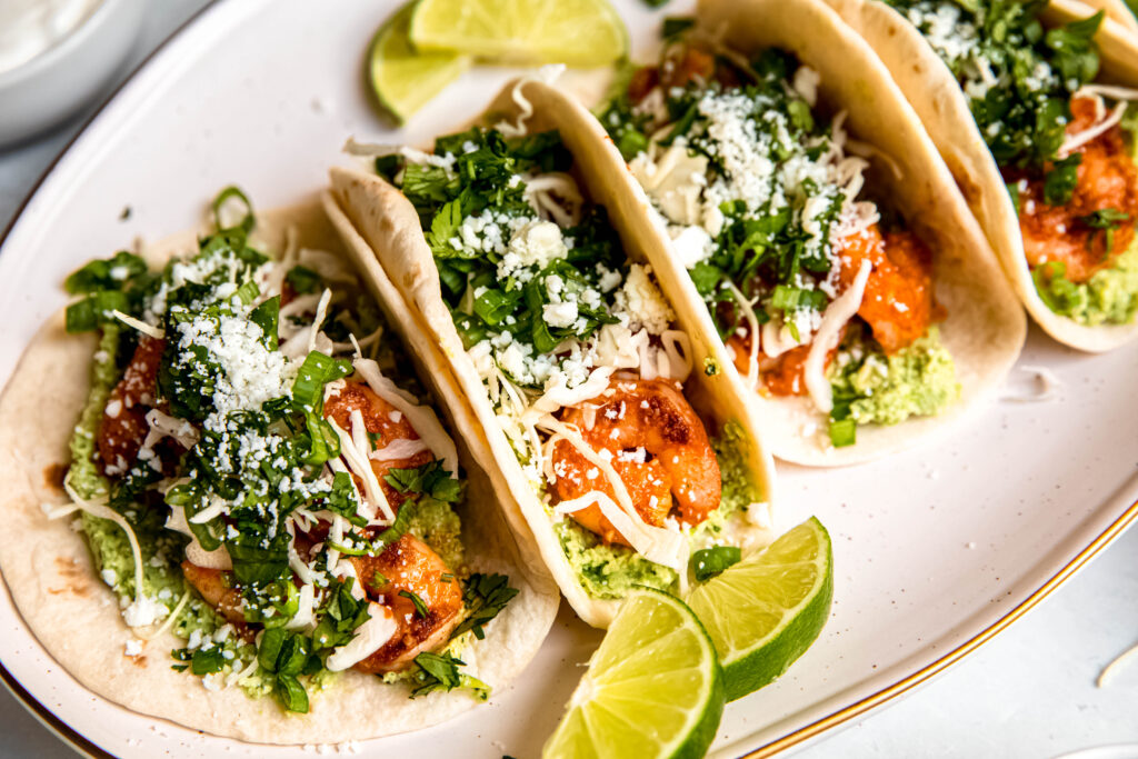 Shrimp Tacos with Edamame Guac and lime wedges on white plate 