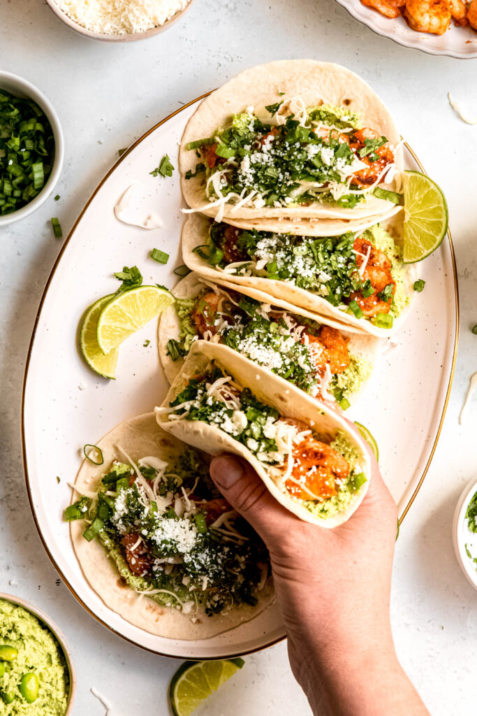 Assembled tacos on white plate with hand holding taco