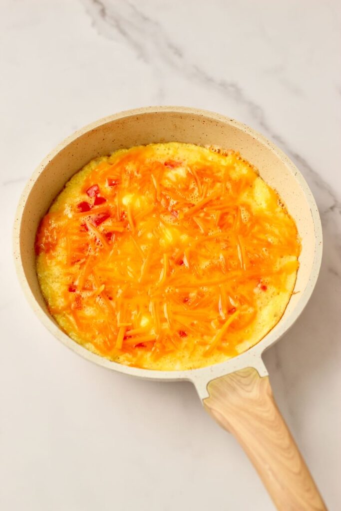 Egg pizza in skillet before fully cooked with cheddar cheese on top 