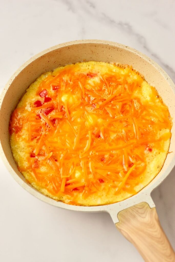 Close up of egg pizza in skillet before fully cooked with cheddar cheese on top 