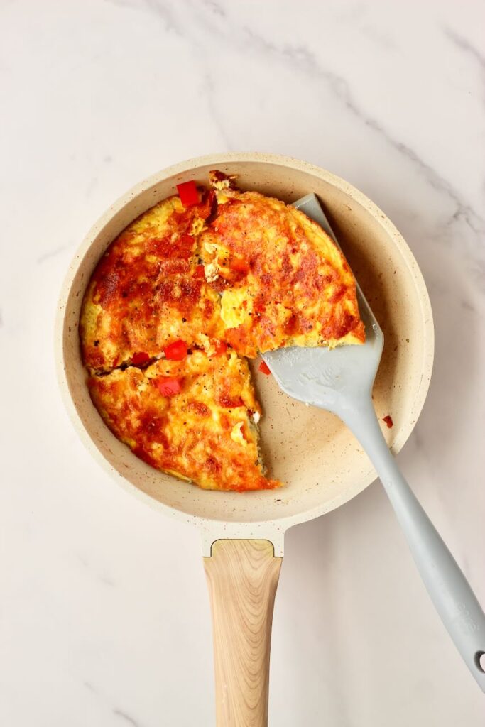 Egg pizza sliced in quarters in skillet with spatula holding piece.
