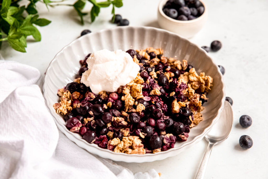 Customizable Fruit Crisp in white bowl and white towel and blueberries in background