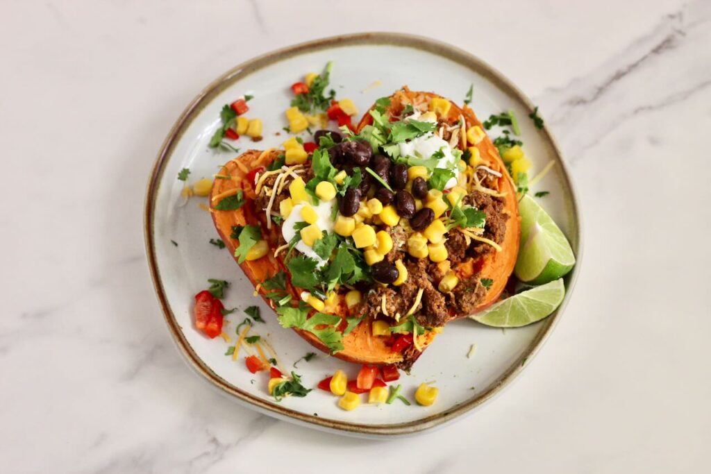 Stuffed Sweet Potato Taco Bar: potatoes with toppings of choice on plate and lime wedges. 