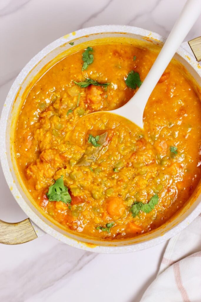 Golden Curry Lentil soup in large pot and white spoon in soup