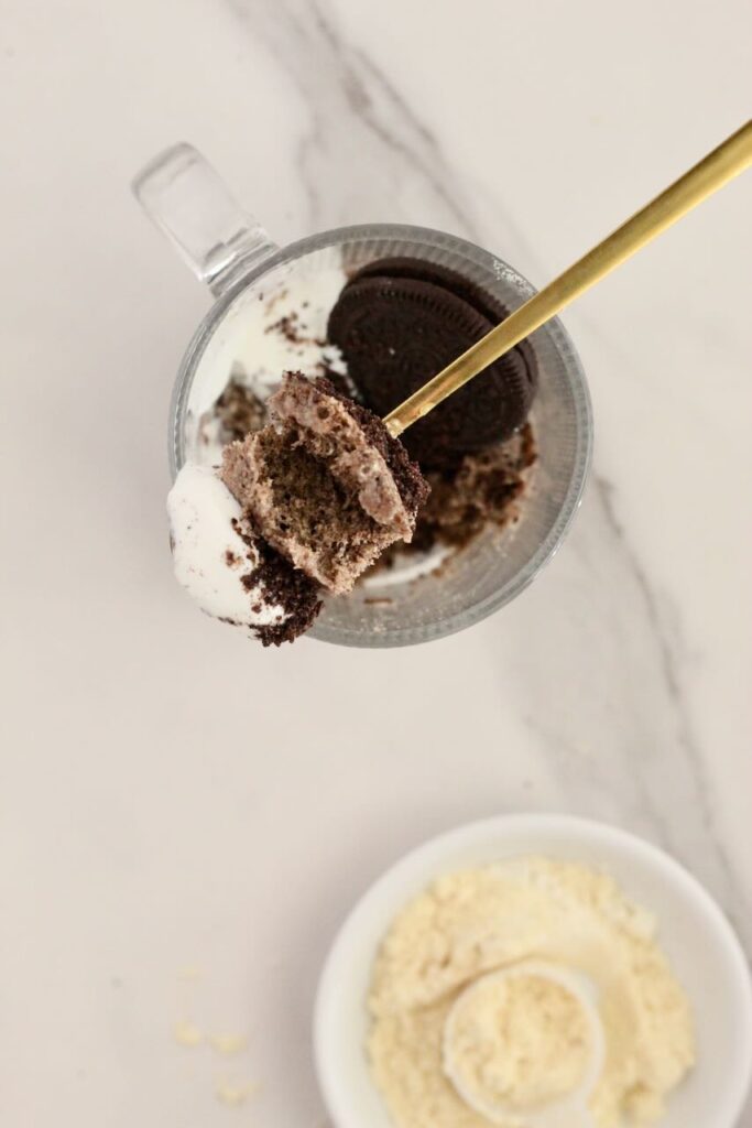 Oreo protein mug cake with gold spoon taking bite out and protein powder in background