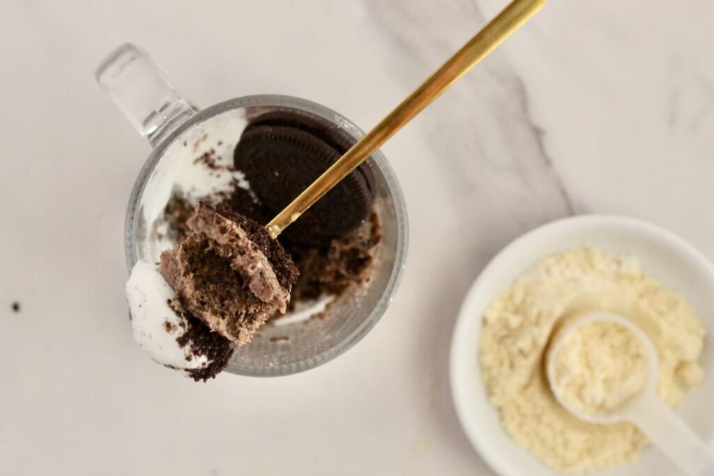 Oreo protein mug cake with gold spoon taking scoop out, with protein powder in background.