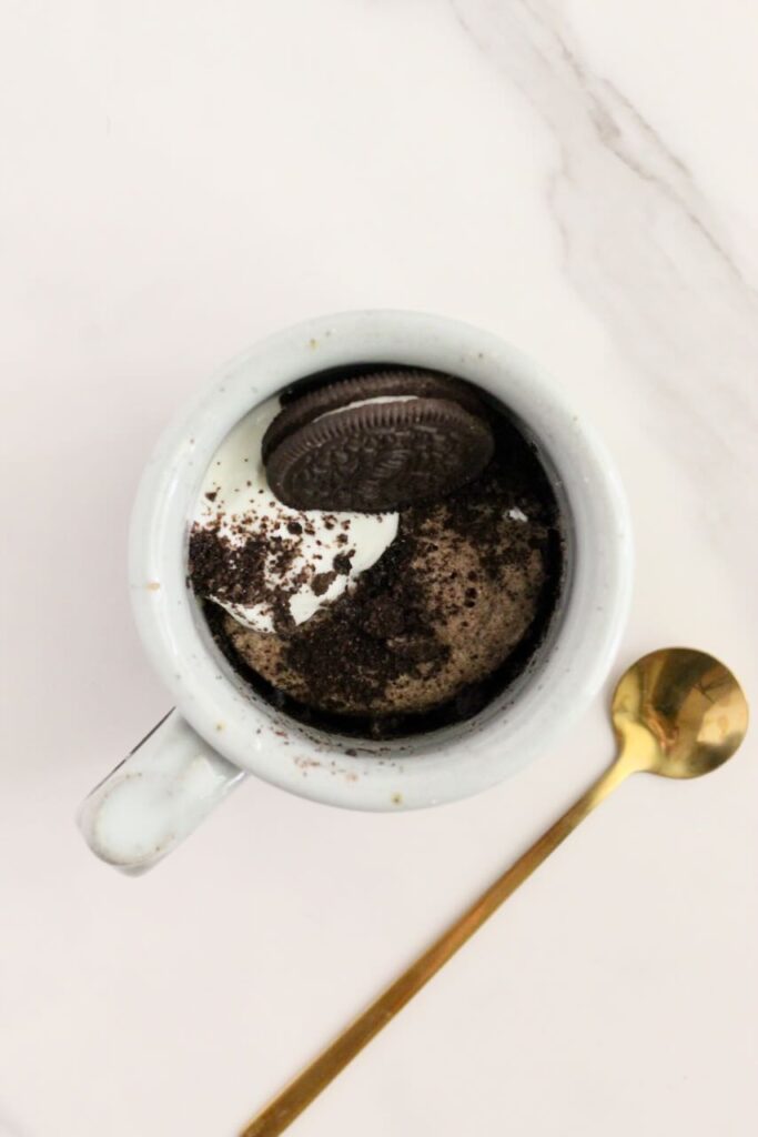 Oreo protein mug cake topped with oreo with gold spoon next to mug